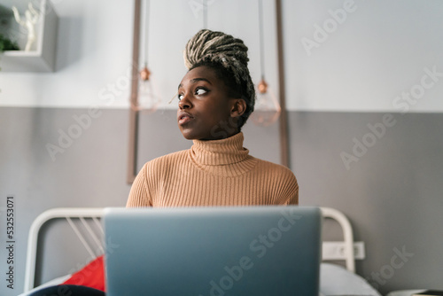 Wistful black woman surfing laptop on bed