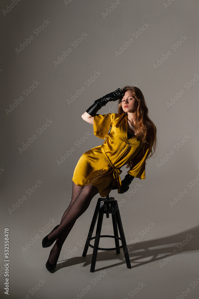 fashion model girl shooting in a mustard-colored dress on a white background on a cyclorama sitting on a chair subdued light fashion model girl shooting in a mustard-colored dress on a white background on a cyclorama sitting on a chair subdued light