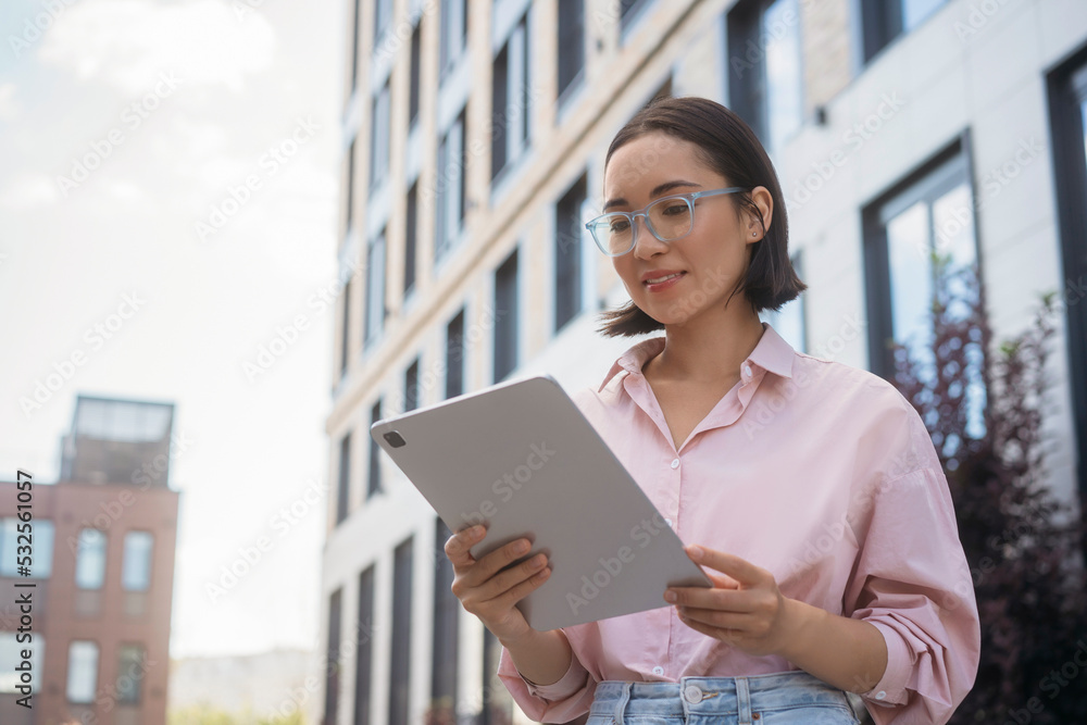 Confident smiling asian student wearing eyeglasses using digital tablet, studying, online education concept. Happy woman reading e-book standing outdoors Confident smiling asian student wearing eyeglasses using digital tablet, studying, online education concept. Happy woman reading e-book standing outdoors