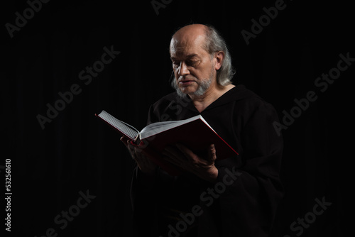 Wallpaper Mural medieval priest in dark robe reading holy bible isolated on black. Torontodigital.ca