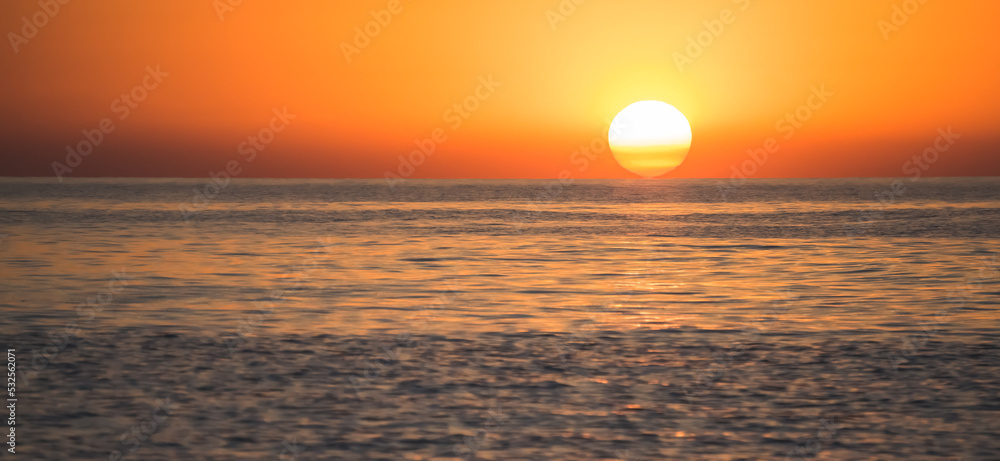 Sunrise of a bright orange sun disk from behind the sea surface of the Black Sea, early cloudless morning