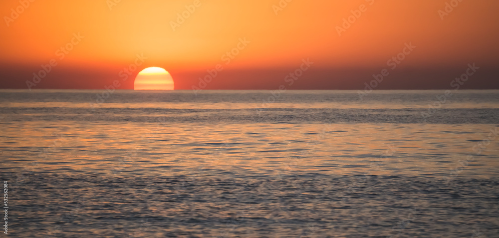Panoramic view of the sun slowly emerging from the horizon of the water surface, the rising of a bright orange sun disk on the Black Sea coast