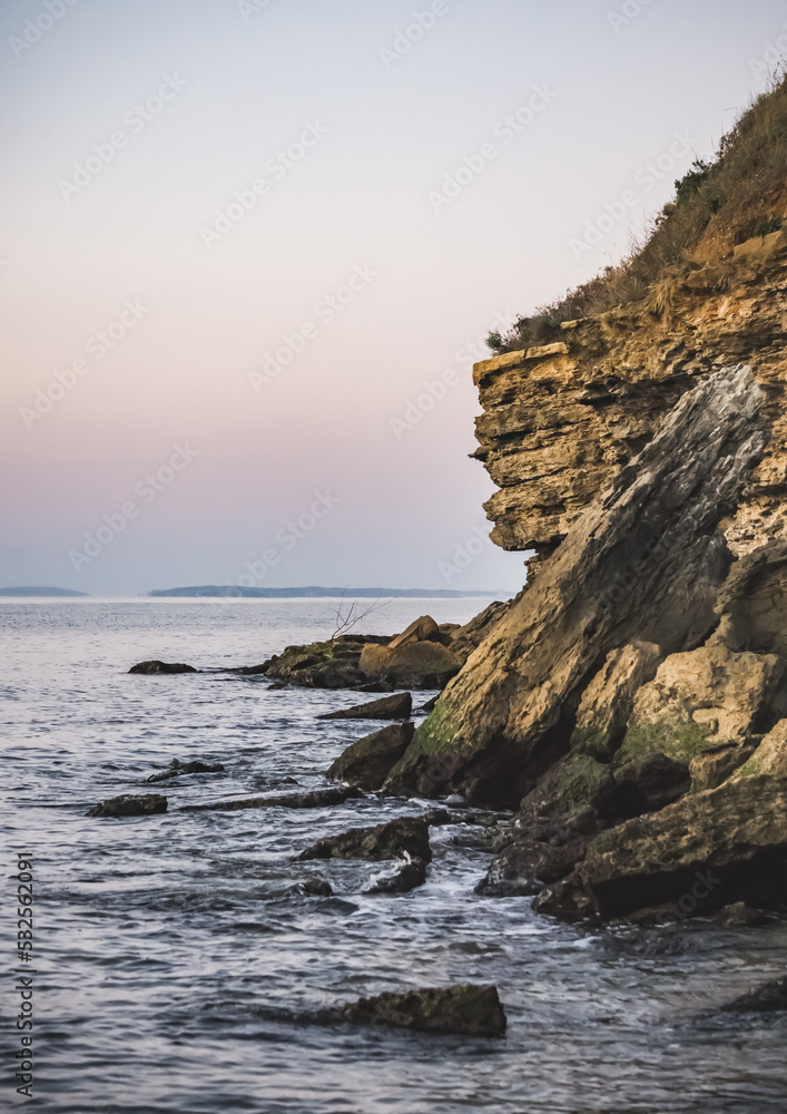 Rocks and pieces of stones, a cliff and a steep coast of the Black Sea against which waves break, soft lighting at dawn