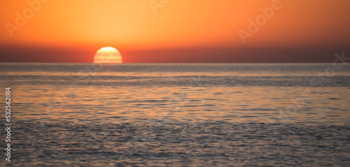 Panoramic view of the sun slowly emerging from the horizon of the water surface, the rising of a bright orange sun disk on the Black Sea coast