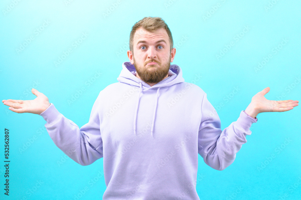 Surprised man in a purple hoodie spreads his hands on a blue background. Casual. Cheerful. Lifestyle. Unknowing. Doubt. Behavior. Shock. Shoulder. Spreading. Amazing. Trouble. Stress. Worry. Reaction Surprised man in a purple hoodie spreads his hands on a blue background. Casual. Cheerful. Lifestyle. Unknowing. Doubt. Behavior. Shock. Shoulder. Spreading. Amazing. Trouble. Stress. Worry. Reaction