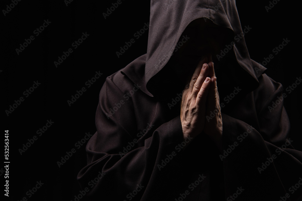anonymous medieval monk in hood praying isolated on black. anonymous medieval monk in hood praying isolated on black.