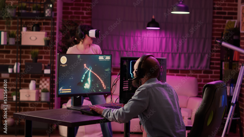 Gamer playing multiplayer space shooter while gaming girl is fighting in virtual reality game at home. Man streaming online action game on pc while gaming girl uses vr goggles for simulation. Gamer playing multiplayer space shooter while gaming girl is fighting in virtual reality game at home. Man streaming online action game on pc while gaming girl uses vr goggles for simulation.