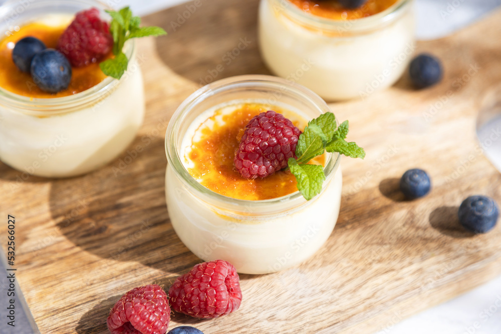 Close-up of a creme brulee dessert garnished with fresh sprig of mint and berries on a cutting board in bright sunshine. Close-up of a creme brulee dessert garnished with fresh sprig of mint and berries on a cutting board in bright sunshine.