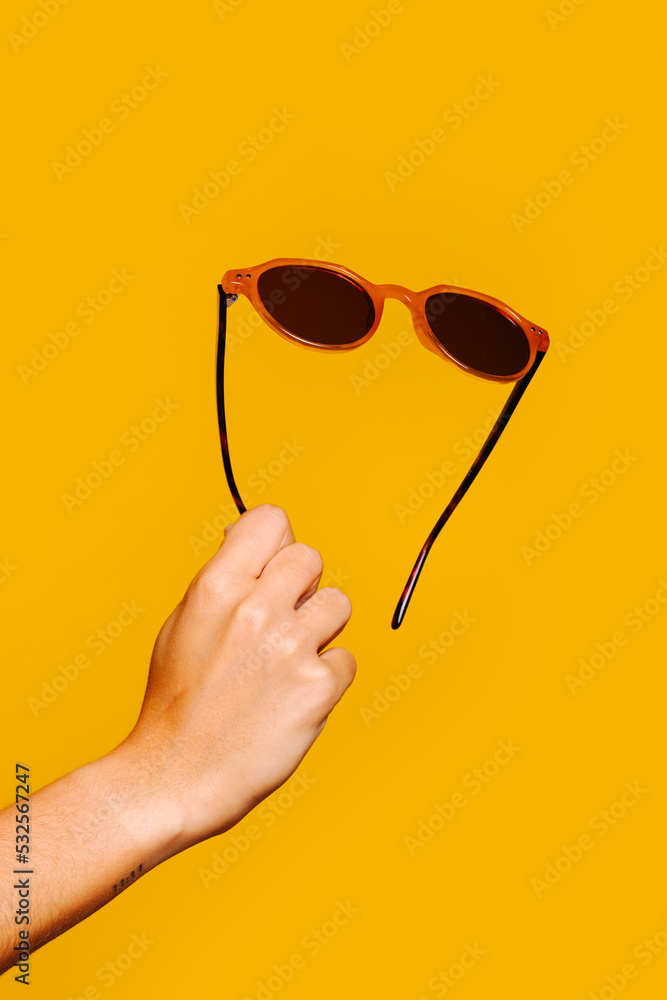 © VICTOR TORRES/Stocksy - Woman's hand holding sunglasses on yellow background