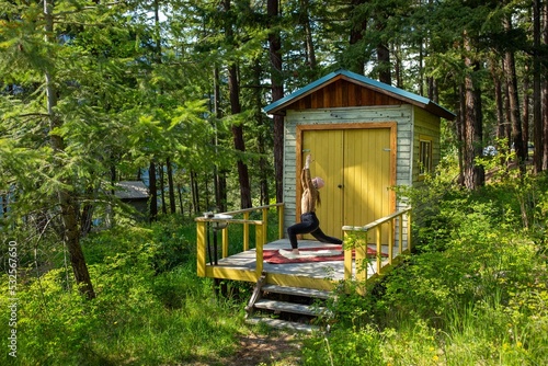 A woman is doing yoga on the balcony of her tiny cabin in the forest. photo