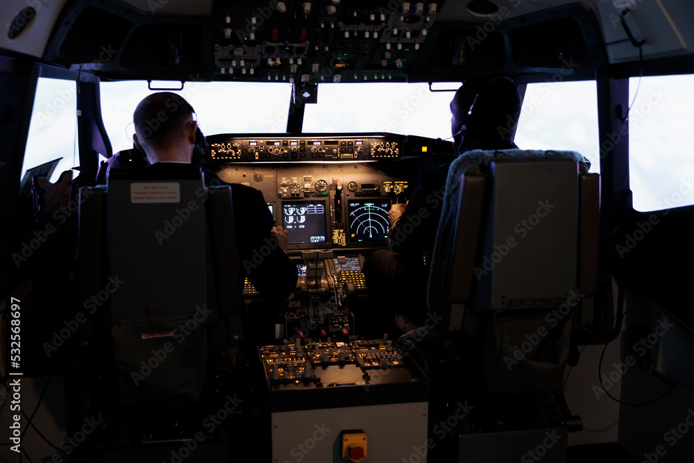 Diverse team of aircrew members using control command to fly plane in aircraft cockpit, pushing power buttons on dashboard. Captain and pilot doing teamwork flying airplane with engine lever. Diverse team of aircrew members using control command to fly plane in aircraft cockpit, pushing power buttons on dashboard. Captain and pilot doing teamwork flying airplane with engine lever.