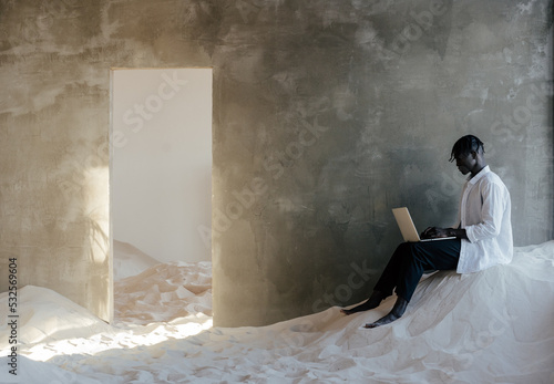 Black man browsing laptop in room with sand photo