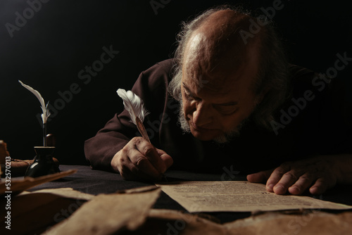 senior abbot writing manuscript on parchment isolated on black. photo
