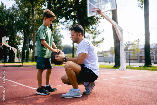Father and son at public basketball court playing basketball.