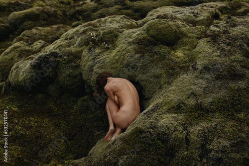 Young slim female in fetal position in the green moss in Iceland photo