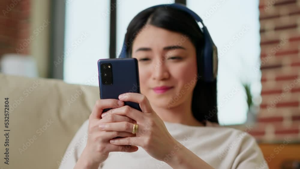 Happy young adult person chatting with friend on smartphone while working remotely. Smiling woman sending text messages on mobile phone while listening to music and doing work from home. Handheld shot Happy young adult person chatting with friend on smartphone while working remotely. Smiling woman sending text messages on mobile phone while listening to music and doing work from home. Handheld shot