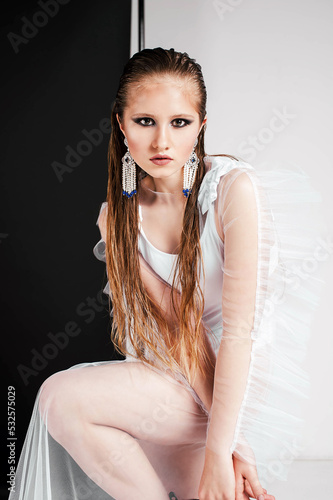 blonde girl in a white bathing suit bodysuit with ruffles in the studio on a white cyclorama with a hairstyle with the effect of wet hair and smokey eye makeup