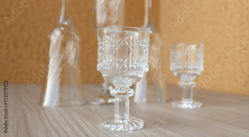Set of empty crystal cups and goblets for wine and other drinks featuring a small adorned goblet in closeup. Glassware for dining, bar, home decor.