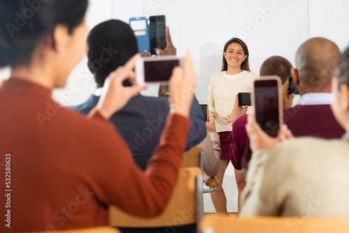 .Students of different age sitting together at tables, shooting lesson on smartphones in classroom