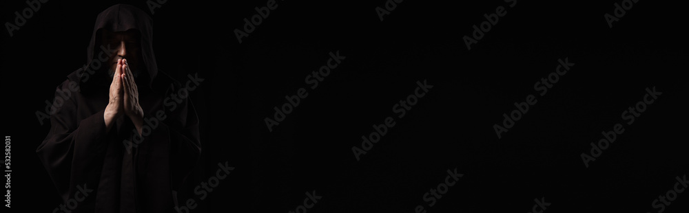 front view of medieval monk in dark hood praying isolated on black, banner. front view of medieval monk in dark hood praying isolated on black, banner.