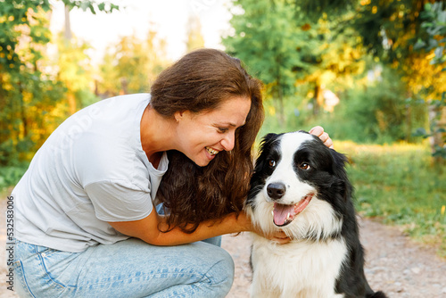 Young attractive woman playing with cute puppy dog border collie on summer outdoor background. Girl kissing holding embracing hugging dog friend. Pet care and animals concept