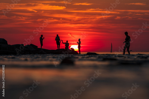 Silhouette of group standing in front of the setting sun on the shore of lake with dog, vibrant sky