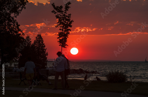 Couple walks in front of setting sun in waterfront park photo