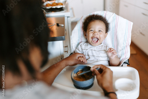 A close up of a father feeding his baby boy in a high chair