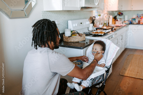 A father feeding his baby boy in a high chair photo