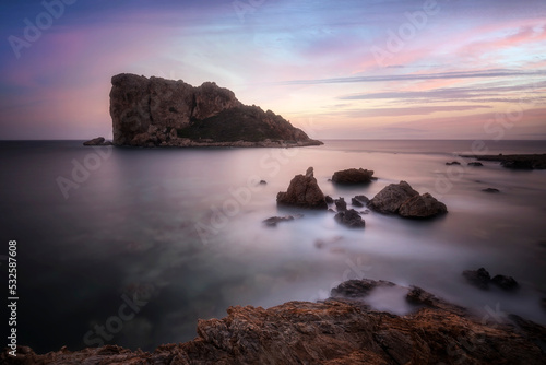 Long exposure photography of an island and rocks, with light the rocks glowing and with clouds and beautiful colored sunset painted sky