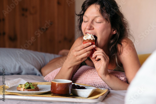 Woman in bed eating a cupcake
