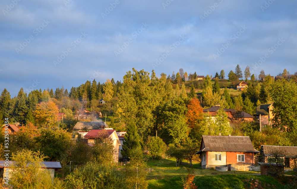 Autumn Carpathian village landscape with guest houses on a mountain slope among colorful trees in the rays of the setting sun. Slavsko, Ukraine Autumn Carpathian village landscape with guest houses on a mountain slope among colorful trees in the rays of the setting sun. Slavsko, Ukraine