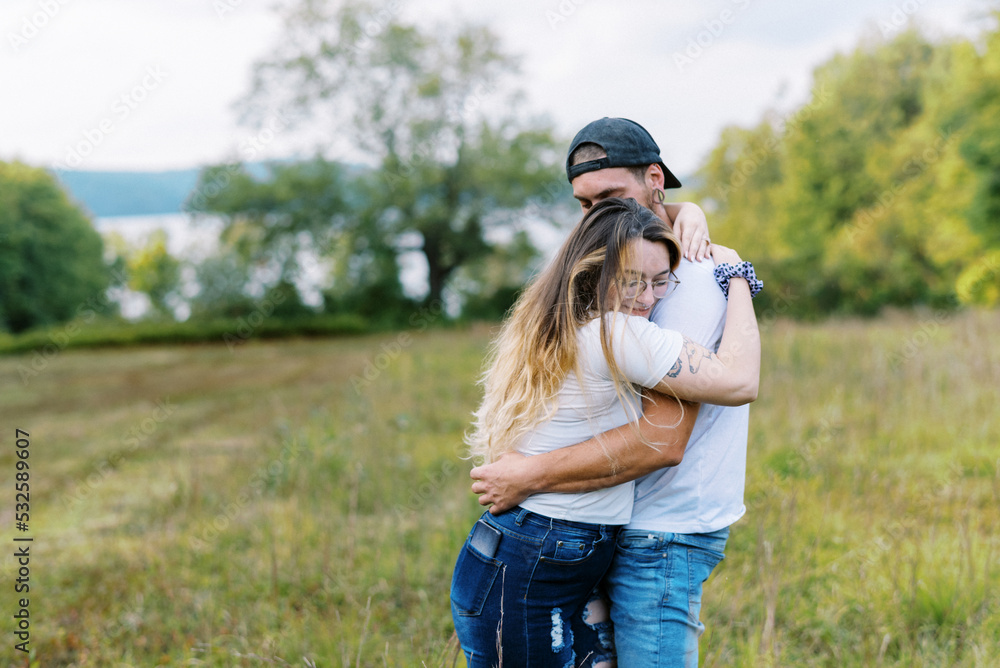 woman and man hugging tightly and leaning on each other in a field ...