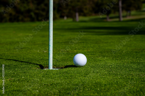 Golf ball on lip of cup on grass background. Golf hole.
