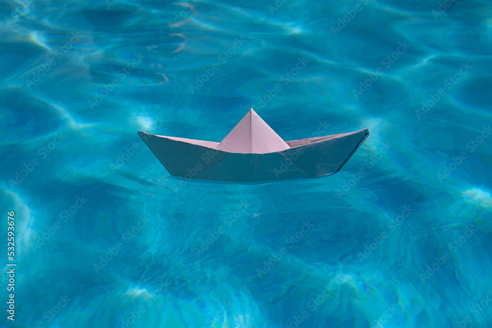 Paper boat sailing on water causing waves and ripples. Paper boat into water. Concept of tourism, travel dreams vacation holiday. Blue water background.