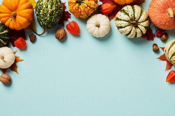Autumn Thanksgiving background. Pumpkins, acorns, walnuts, physalis and maple leaves on pastel blue table top view.