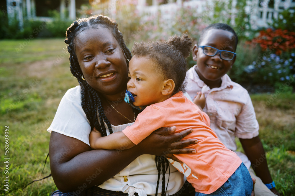 Happy smiling mother sitting in grass with her children in summer Happy smiling mother sitting in grass with her children in summer