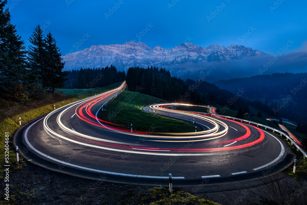 Light Trail Of Moving Cars Driving Up A Panoramic Serpentine Road In The Swiss Alps - obrazy, fototapety, plakaty 