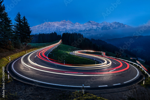 Billede på lærred Light Trail Of Moving Cars Driving Up A Panoramic Serpentine Road In The Swiss A