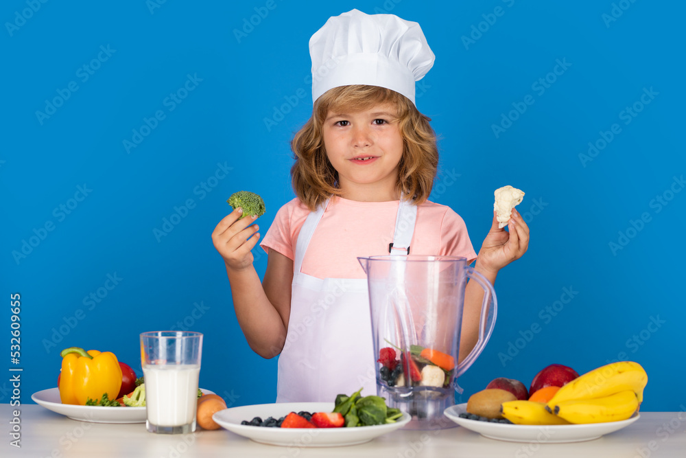 Child wearing cooker uniform and chef hat hold broccoli preparing vegetables on kitchen, studio portrait. Cooking, culinary and kids food concept. Child wearing cooker uniform and chef hat hold broccoli preparing vegetables on kitchen, studio portrait. Cooking, culinary and kids food concept.