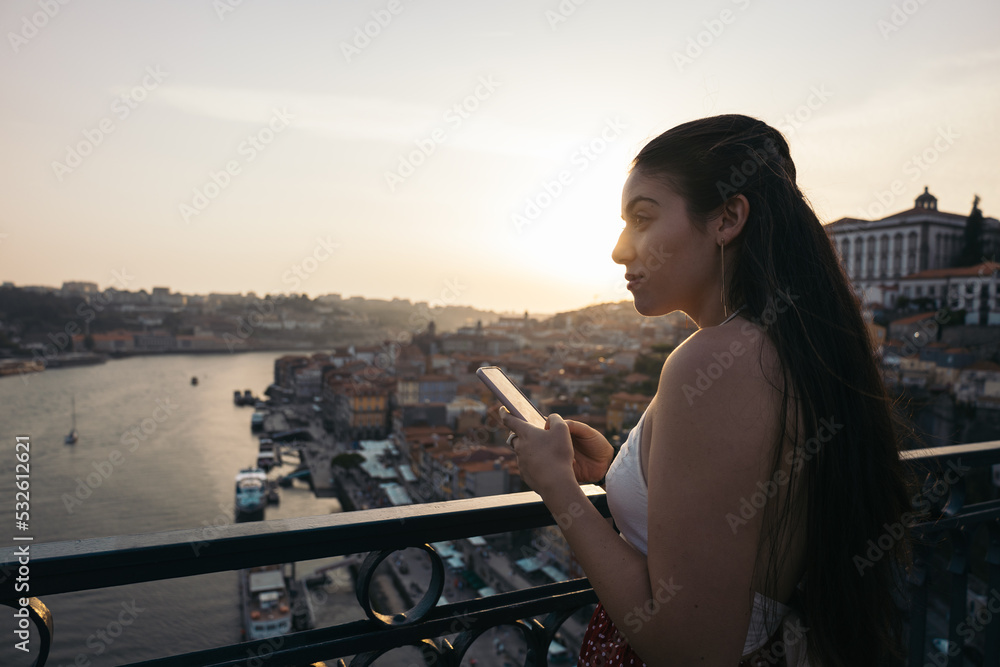 Young woman using smartphone and watching the city from the bridge Young woman using smartphone and watching the city from the bridge