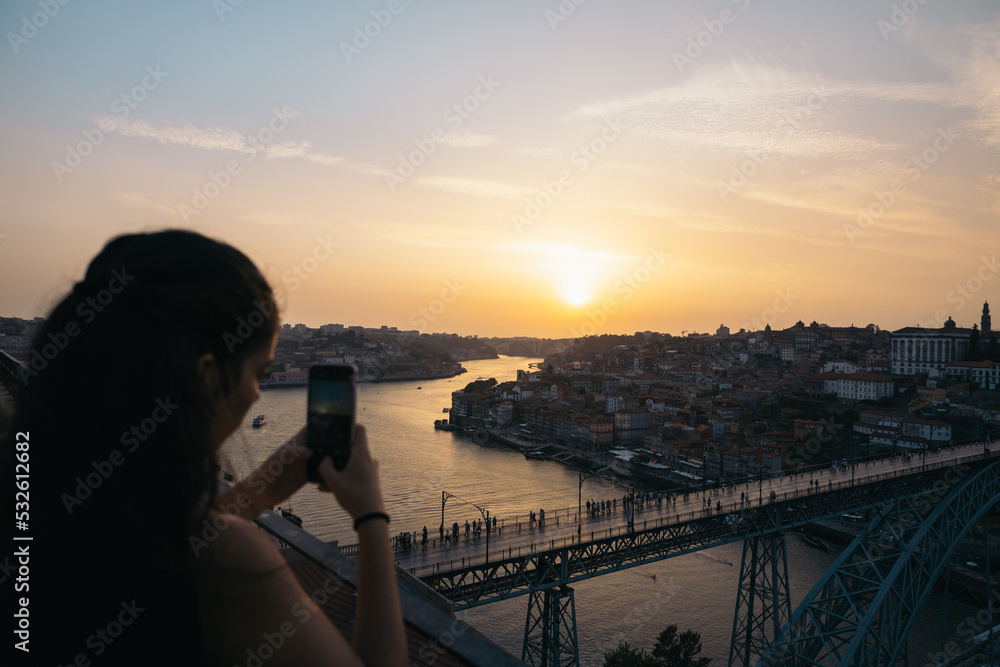 © Pedro Merino/Stocksy - Young woman taking pictures with smartphone of the sunset in Porto