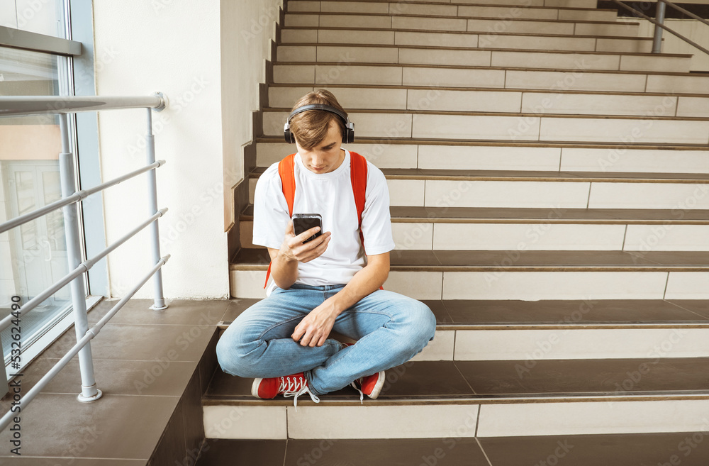 Student with smartphone sits on the steps indoors. Selective focus