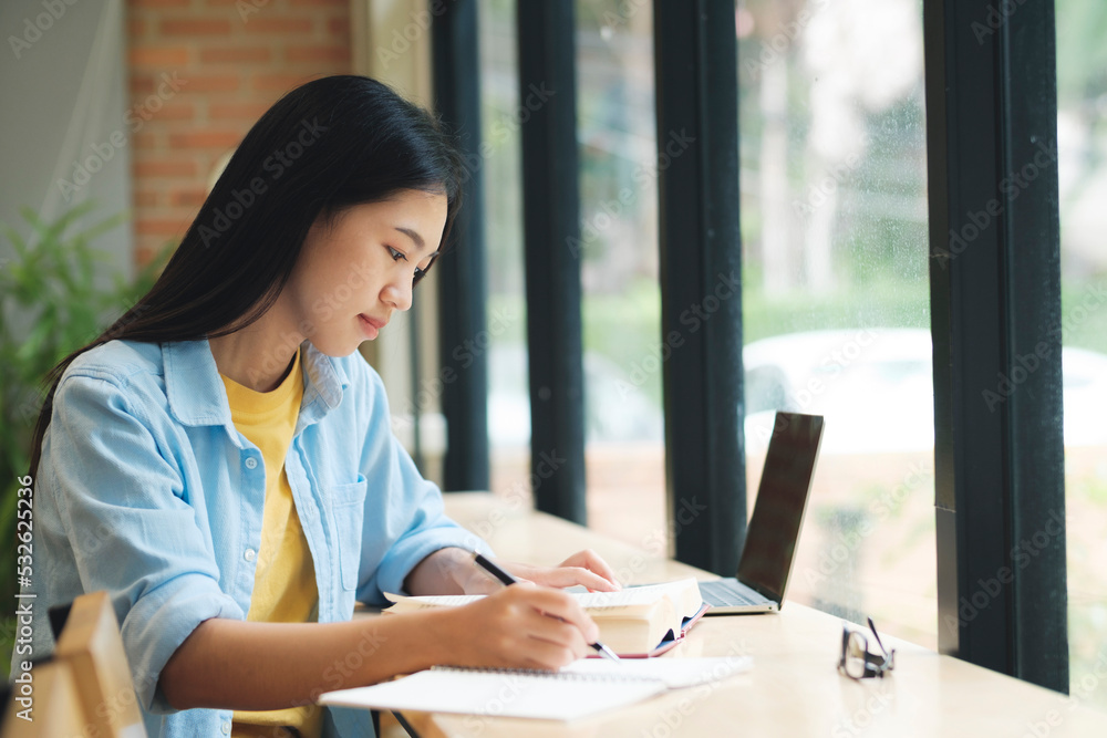 Young asian woman sitting at table and writing on notebook. Young asian woman sitting at table and writing on notebook.