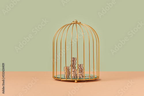 Golden birdcage with stacks of coins inside. photo