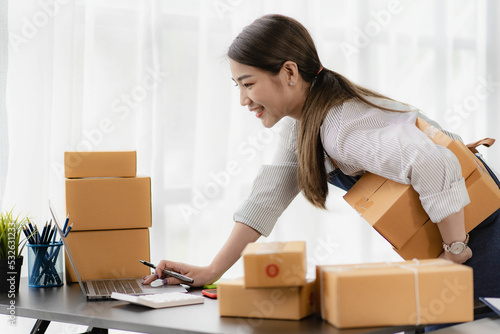 beautiful asian woman working at home selling online with yellow box and laptop on taking name orders from customers sme business concept parcel delivery © ArLawKa