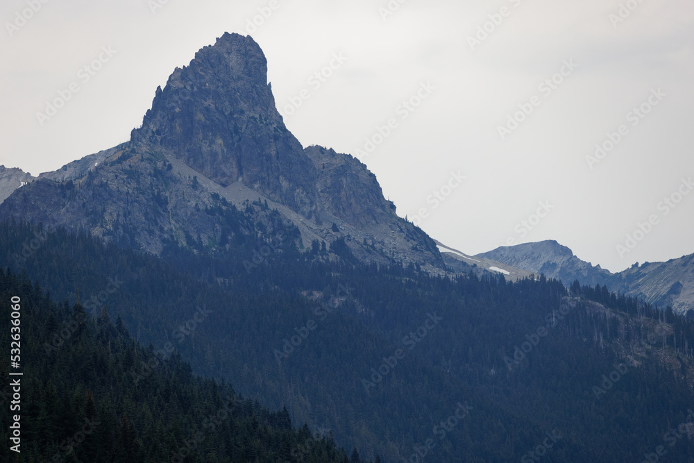 A mountain peak under a hazy grayish-white sky in Okanogan Wenatchee National Forest, Washington.