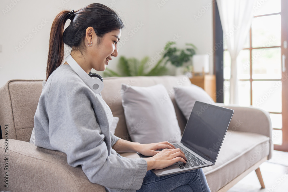 An business Asian woman working at home, chatting online with a colleague on her laptop and wear headphones while on the couch in living room at home. An business Asian woman working at home, chatting online with a colleague on her laptop and wear headphones while on the couch in living room at home.