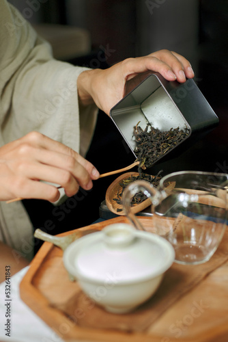 Women's hands put dry Chinese tea leaves into a wooden chahe photo