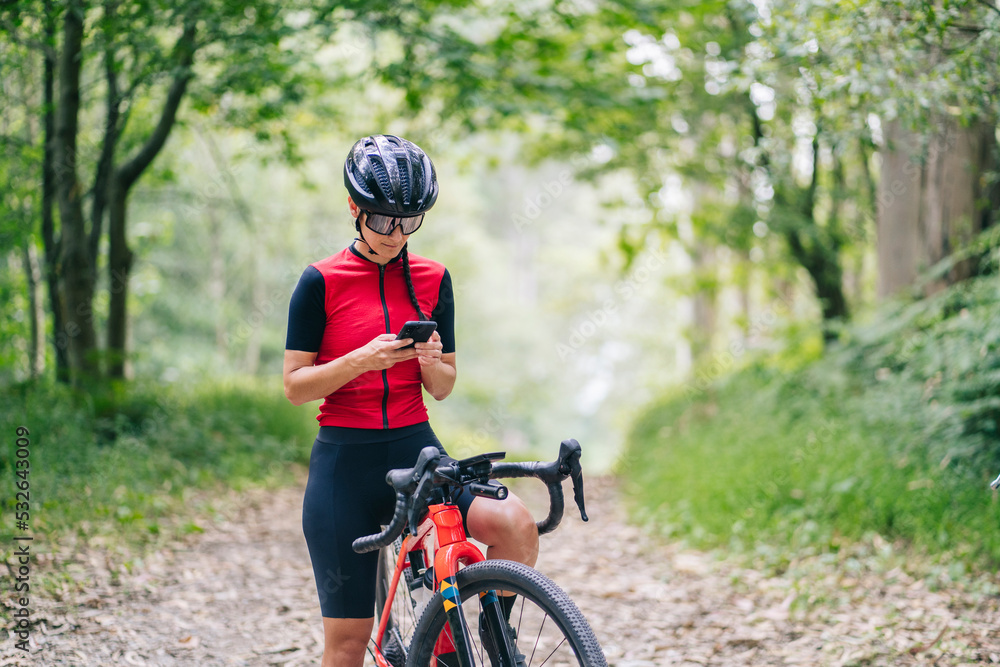 Fit lady using smartphone on bicycle in forest Fit lady using smartphone on bicycle in forest